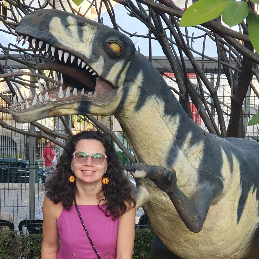 No fundo da foto o dinossauro rex e na frente dele a aluna Michelly sorrindo